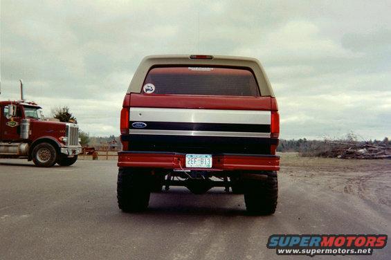 Rear view of a lifted red and tan Ford Bronco with a large semi-truck to its left