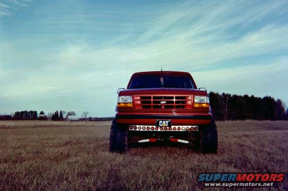 Red Ford F-Series truck with a "CAT" license plate and auxiliary lights parked in a field