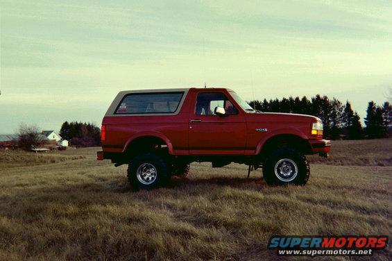 Red lifted Ford Bronco side view in a grassy field