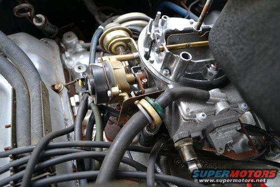 Close-up of a vehicle's carburetor and engine components, with various hoses and wires visible