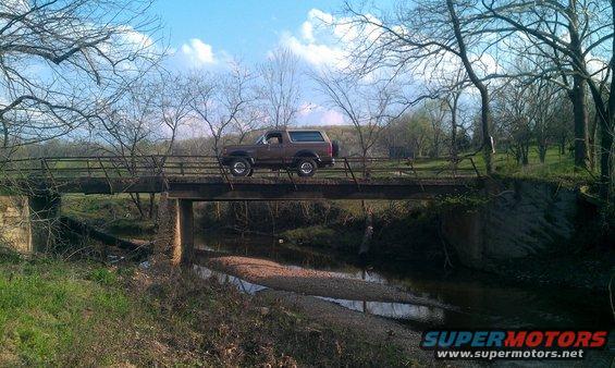 Brown 1987 Ford Bronco driving across a rural bridge