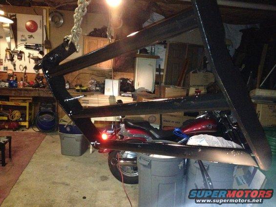 Motorcycle parked in garage, partially obscured by a large metal frame hanging from a chain