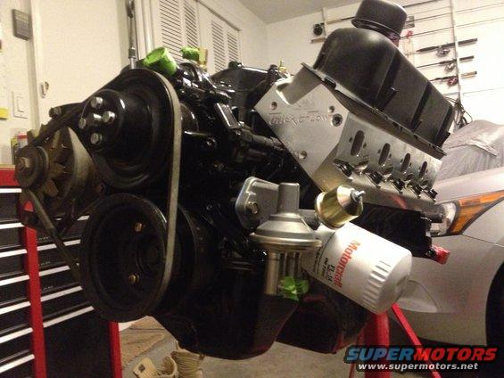 Black V8 engine on a red stand, with a silver car partially visible behind it