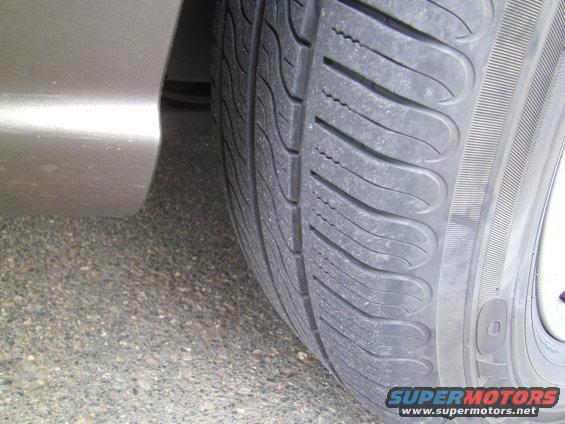 Close-up of a worn tire next to a beige car fender