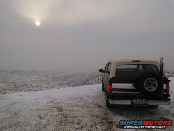 Rear view of a 1992 Ford Bronco with a spare tire on the back, parked on a snowy hill