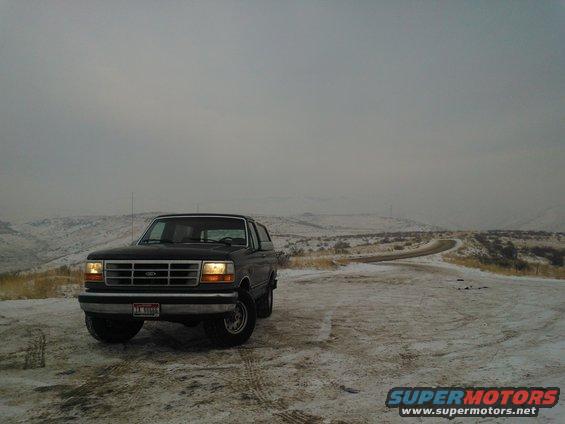 Black Ford Bronco parked on a snowy dirt road with hills in the background