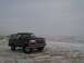 1992 Ford Bronco - A dark 1992 Ford Bronco with a white top is parked on a snowy road with hills in the background.