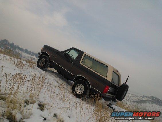 1992 Ford Bronco climbing a snow-covered incline with dry grass