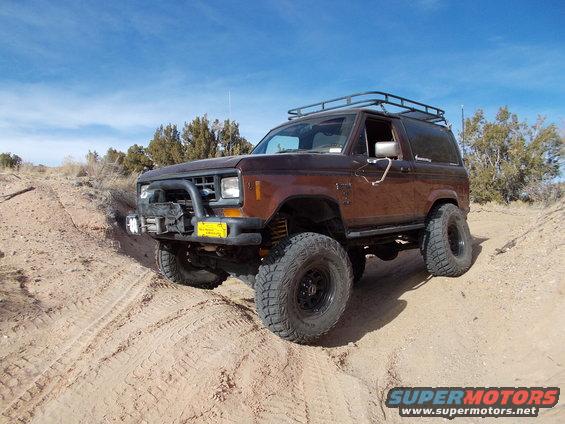 Brown Ford Bronco II with roof rack and bull bar on sandy terrain