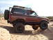 1986 Ford Bronco II - This lifted 1986 Ford Bronco II navigates a sandy incline, equipped with large off-road tires and a roof rack.