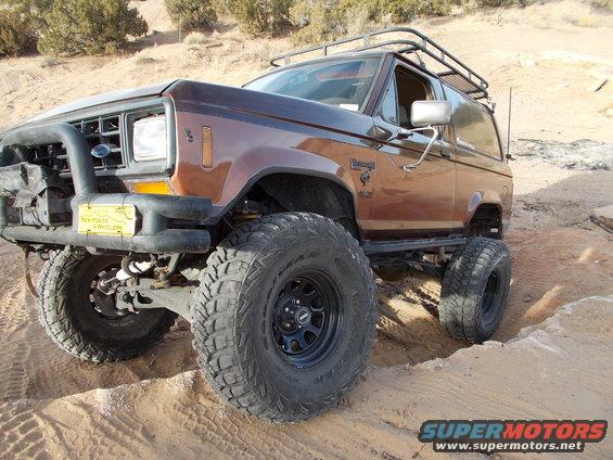 Brown 1986 Ford Bronco II with large tires and a roof rack on a dirt trail