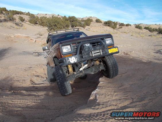 Brown Ford Bronco II with off-road tires navigating a sandy incline