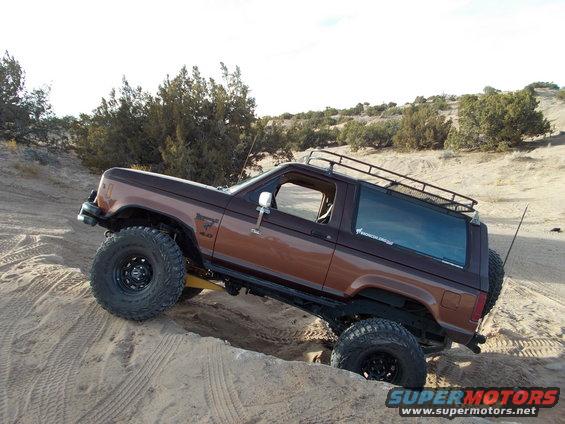 Brown Ford Bronco II with lifted suspension and large tires driving on a sandy incline