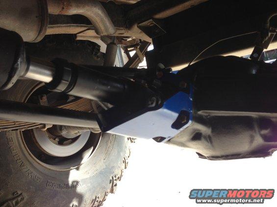 Underside view of a vehicle's suspension and drive shaft with a large tire visible