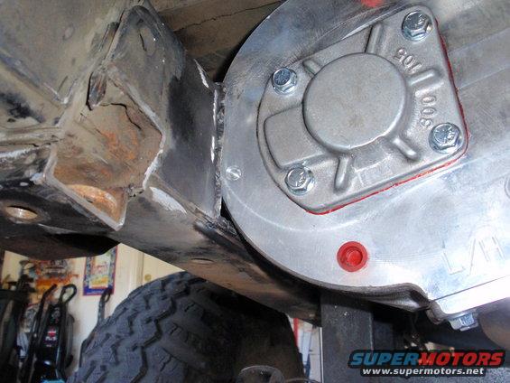 Close-up of a modified transfer case attached to vehicle frame with new welds. Tire visible below