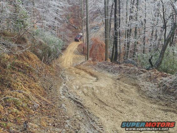 Off-road vehicle climbing a steep, muddy hill in a wooded area with icy trees