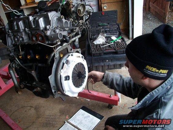 Engine on stand with mechanic looking at it, toolbox open nearby