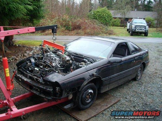 Black coupe with engine removed by a red engine hoist