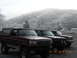 1986 Ford Bronco - Three Ford Broncos are parked in a line on a foggy day, with a mountain range in the background.