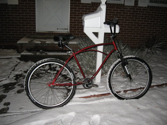 Red bicycle with wide tires parked in snow next to a white mailbox