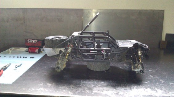 RC rock crawler on a workbench with tools and parts nearby. It has a roll cage and exposed suspension