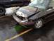 1988 Ford Bronco - A black sedan with significant front-end damage is parked next to a black SUV in a wet parking lot.