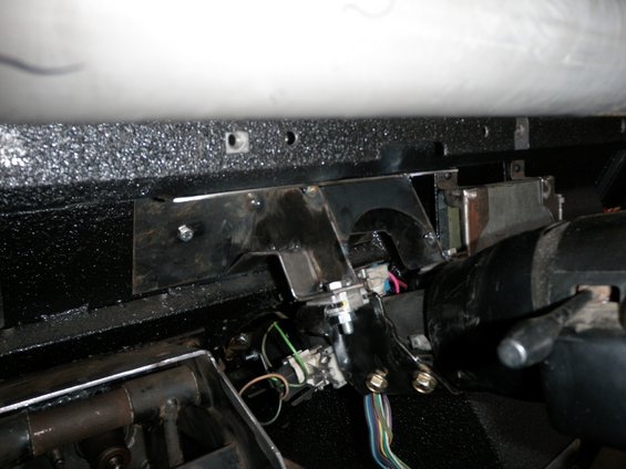 Close-up of a custom metal bracket attached to a vehicle's steering column, with visible wiring harnesses