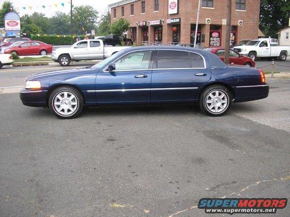 Blue sedan parked on asphalt, side view. Chrome trim along the bottom of the doors and windows. Multi-spoke alloy wheels