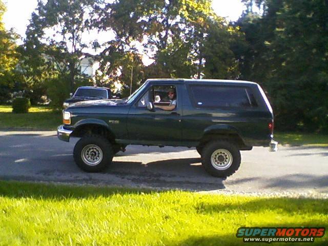 Green Ford Bronco with lifted suspension and aftermarket wheels, seen from the side