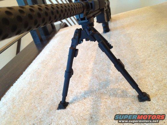 Black machine gun bipod with perforated barrel shroud