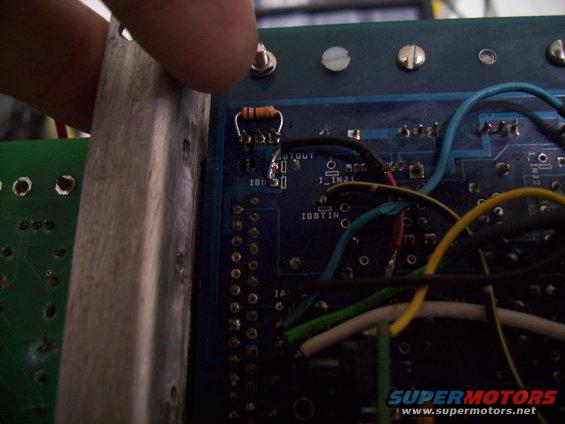 Close-up of a circuit board with a resistor and wires, a finger is touching a metal heatsink