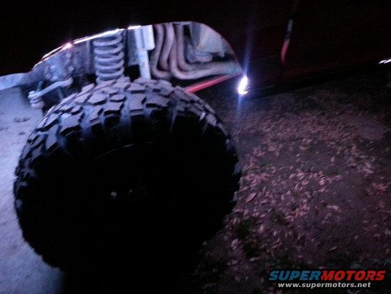 Close-up of a large off-road tire and suspension components, with undercarriage lights visible