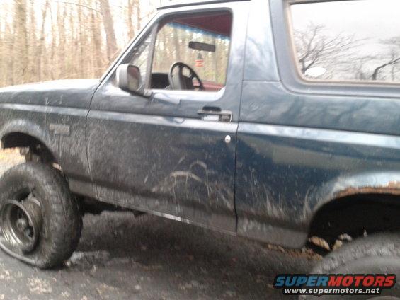 Side view of a dark blue 1995 Ford Bronco with a flat tire and muddy body