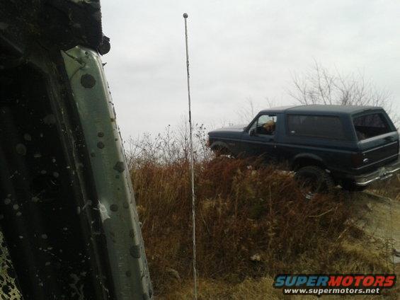 Dark blue SUV, possibly a Ford Bronco, on a grassy incline. Visible text 'SUPERMOTORS'