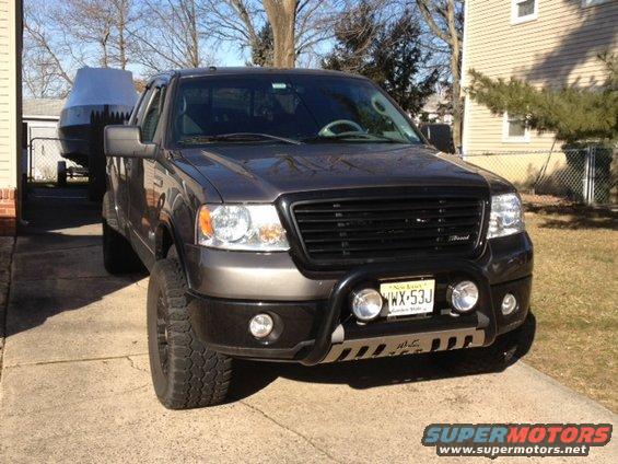 Dark gray Ford F-150 truck with a black grille and bull bar, towing a boat covered with a gray tarp