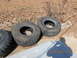 1986 Ford Bronco - Several large off-road tires are laid out on the ground next to some dry brush and fallen leaves.