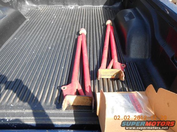 Two red suspension control arms and a box of parts in a truck bed