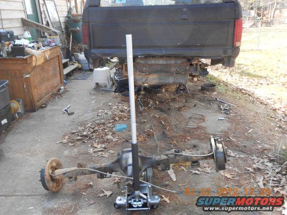 Truck frame with rear axle assembly removed and on a jack. Tools and debris are scattered around