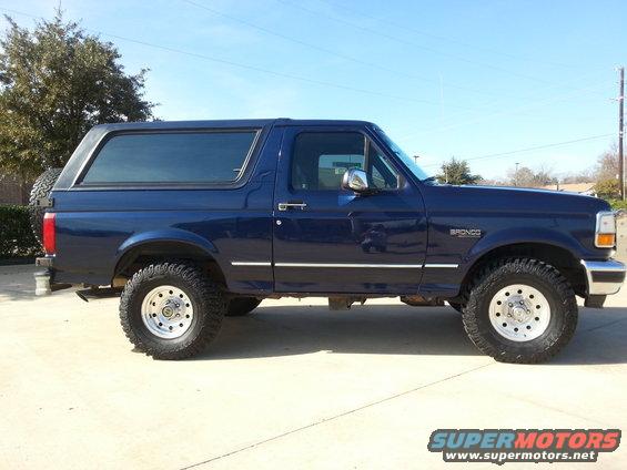 Blue Ford Bronco SUV, side view, lifted suspension, aftermarket wheels, spare tire on rear door