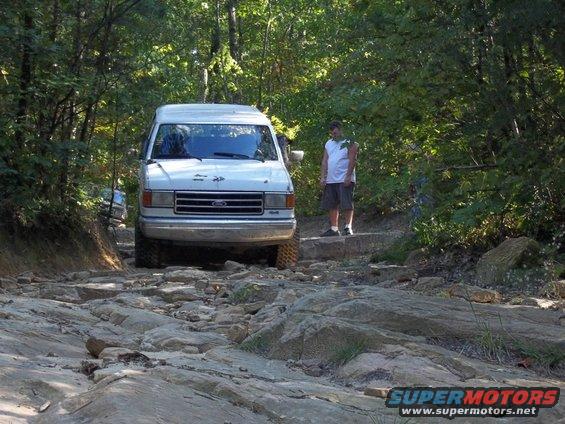 White 1990 Ford Bronco on a rocky trail, front view. A man stands on a step to the right