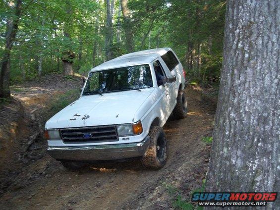 White 1987 Ford Bronco driving on a dirt trail in a forest