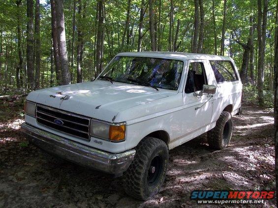 White 1990 Ford Bronco parked on a dirt path in a forest