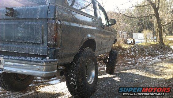 1995 Ford Bronco rear view, lifted with large tires, on a gravel road with snow patches