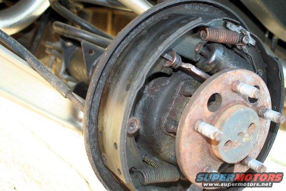 Close-up of a rusty rear drum brake assembly with brake shoes and springs visible