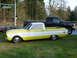 1961 Ford Ranchero - A two-tone yellow and white pickup truck is parked on grass next to a black pickup truck.