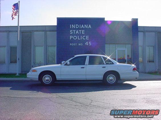 White police sedan parked in front of Indiana State Police Post No. 45. The car appears to be a 1998 model