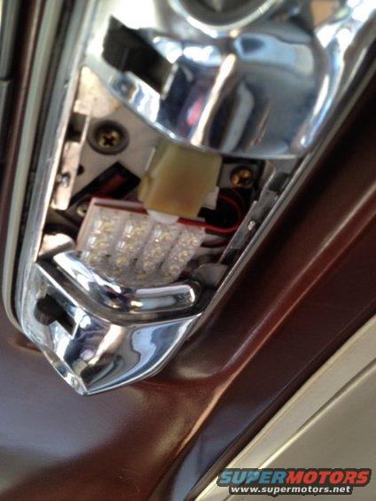 Chrome trim surrounds a modern LED light fixture installed in a car's dark brown interior panel