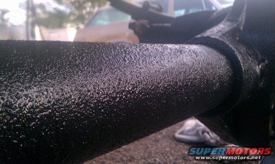 Black textured metal pipe with suspension component, blurry vehicle in background