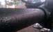 1995 Ford Bronco - Close-up of a black textured metal pipe and suspension component with a blurry vehicle in the background.