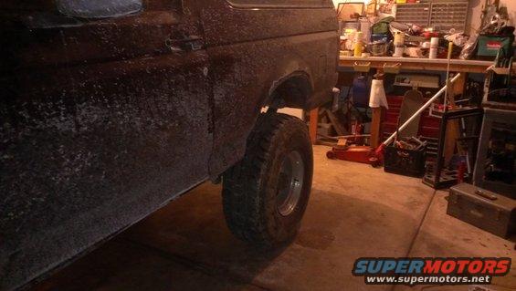 Rear quarter panel and tire of a dark-colored Ford Bronco, possibly from the 1980s, in a garage